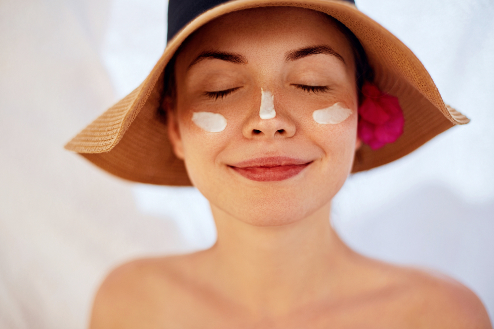 Una mujer sonríe aplicando crema de sol en la cara.